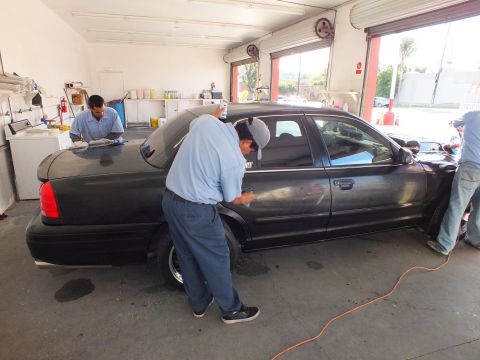 2003 Ford Crown Victoria - Workers clean the side of a black Ford Crown Victoria parked inside a detailing garage.