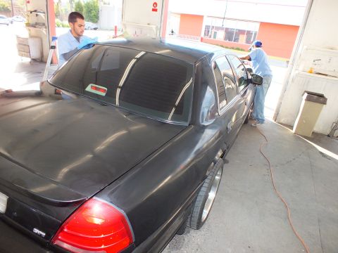 2003 Ford Crown Victoria - Worker dries the rear of a black Crown Victoria sedan inside an open detail bay.