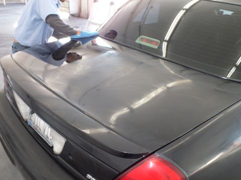2003 Ford Crown Victoria - Glossy black trunk and rear glass of a sedan reflect overhead light during detailing.