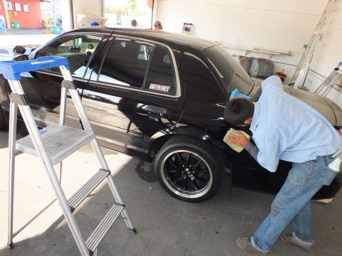 2003 Ford Crown Victoria - Detailer buffs the rear quarter of a black Crown Victoria beside a step ladder.