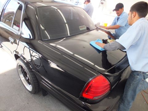2003 Ford Crown Victoria - Detailer wipes the trunk of a black Crown Victoria beside its rounded red taillight.