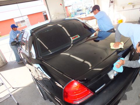 2003 Ford Crown Victoria - Detailers towel the trunk and back window of a black Crown Victoria sedan in a garage.