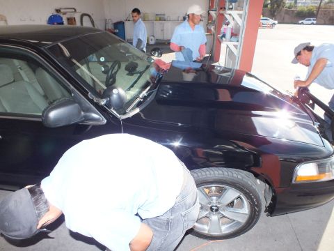 2003 Ford Crown Victoria - Workers clean the hood and front fender of a black Crown Victoria in a garage bay.