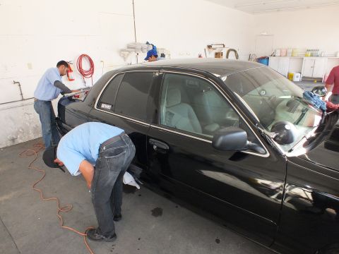 2003 Ford Crown Victoria - Worker bends to clean the lower door of a black Crown Victoria inside a detail bay.