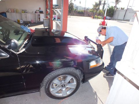 2003 Ford Crown Victoria - Detailer wipes the front headlight and hood of a black Crown Victoria in a garage.