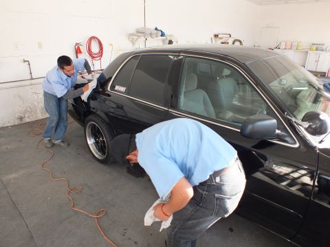 2003 Ford Crown Victoria - Detailers clean the fender and door of a black Crown Victoria on black wheels in a shop.