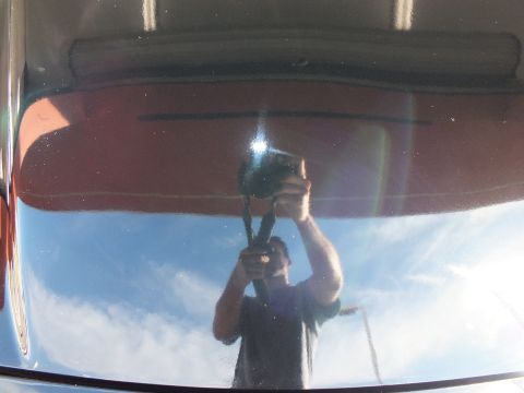 2003 Ford Crown Victoria - Sky and a phone photographer reflected on the mirror-finish black hood of a car.