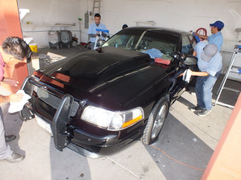 2003 Ford Crown Victoria - Shop staff wipe down the front fender and hood of a black Crown Victoria with a push bar.