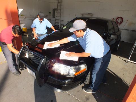 2003 Ford Crown Victoria - Detailers in blue shirts buff the hood and front clip of a black Crown Victoria sedan.