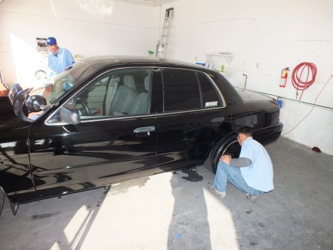 2003 Ford Crown Victoria - Worker tends the rear wheel along the driver side of a black four-door Crown Victoria.