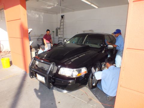 2003 Ford Crown Victoria - Crew surrounds a black Crown Victoria fitted with a front push bar inside a detail garage.