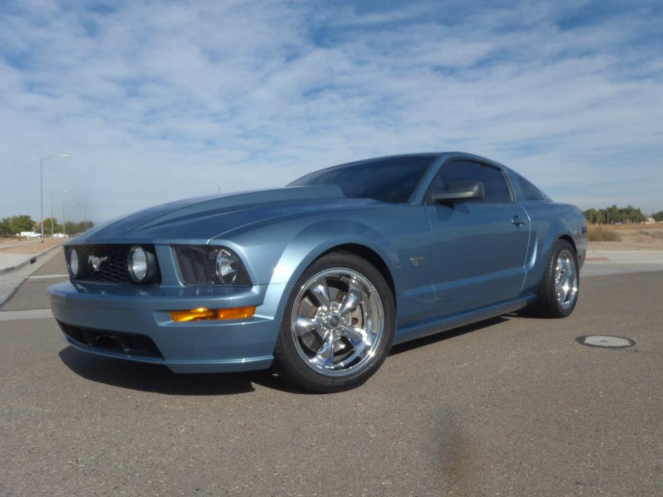 Blue Ford Mustang coupe with aftermarket wheels parked on asphalt