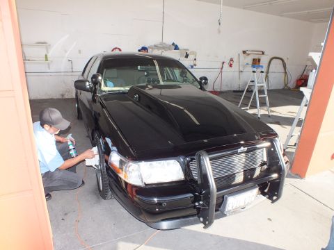 2003 Ford Crown Victoria - Technician crouches at the front wheel of a black Crown Victoria with a chrome push bar.
