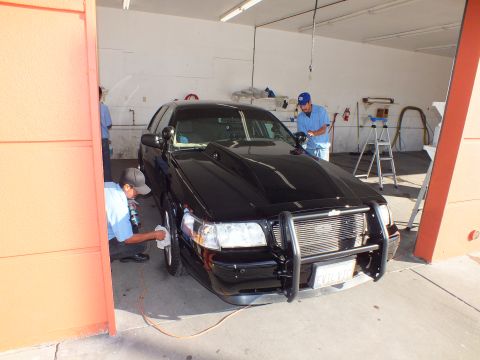 2003 Ford Crown Victoria - Two detailers work the front wheel and door of a black Crown Victoria with a grille guard.