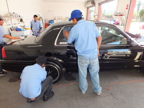 2003 Ford Crown Victoria - Detailer in a blue cap works the rear side window of a black sedan while another cleans a wheel.