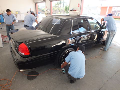 2003 Ford Crown Victoria - Crew buffs the rear quarter and wheel of a black Crown Victoria inside an open detail shop.