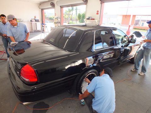 2003 Ford Crown Victoria - Black Crown Victoria viewed from the rear corner as a worker cleans the rear wheel.
