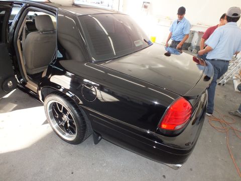 2003 Ford Crown Victoria - Black Crown Victoria with rear door open and aftermarket multi-spoke wheels in a shop.