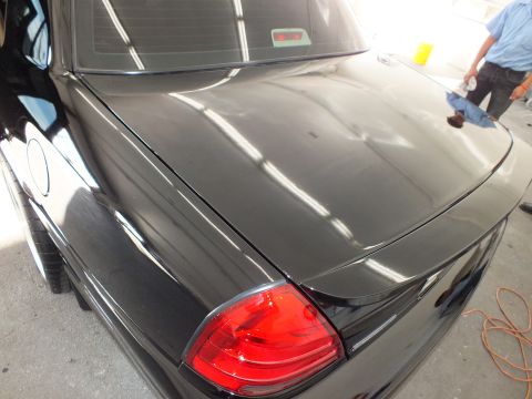 2003 Ford Crown Victoria - Glossy black trunk lid and red tail light of a detailed sedan with a worker behind it.