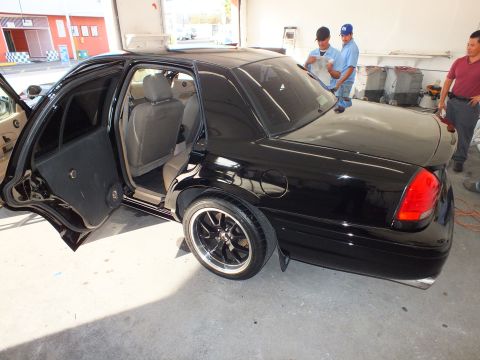 2003 Ford Crown Victoria - Black Crown Victoria seen from rear corner with door open and detail crew standing by.