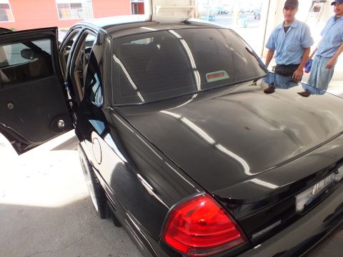 2003 Ford Crown Victoria - Tinted rear glass and trunk of a black Crown Victoria with two workers standing behind.