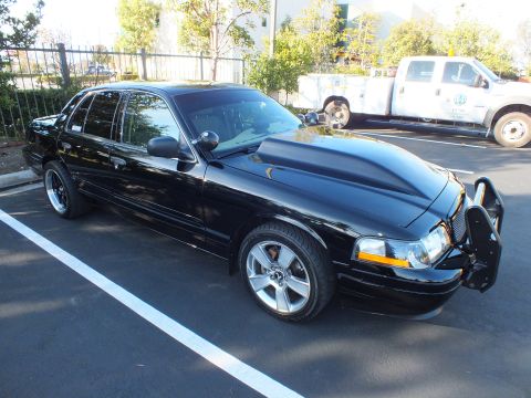 2003 Ford Crown Victoria - Modified black sedan showing raised hood scoop and front push bar, parked outdoors