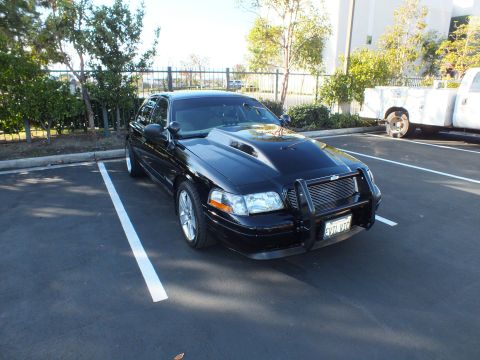 2003 Ford Crown Victoria - Front of a black sedan with grille guard and cowl hood angled in a parking stall
