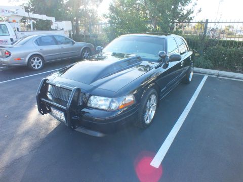2003 Ford Crown Victoria - Angled front view of a black full-size sedan with billet grille and push bar