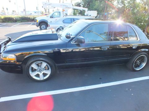 2003 Ford Crown Victoria - Rear quarter of a black full-size sedan parked near a utility truck