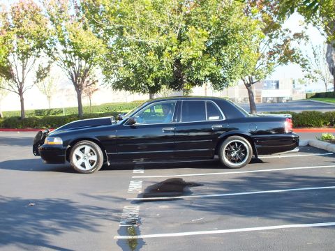 2003 Ford Crown Victoria - Side profile of a black full-size sedan parked under trees in daylight