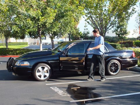 2003 Ford Crown Victoria - Person stands at the open door of a black modified sedan in a sunny parking lot