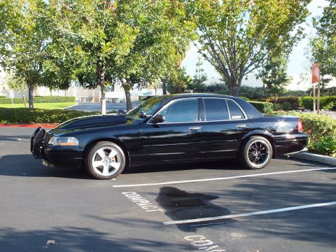 2003 Ford Crown Victoria - Angled front view of a black full-size sedan parked under trees