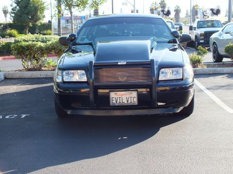 2003 Ford Crown Victoria - Front view of a black modified sedan in a parking lot with work trucks behind