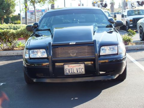 2003 Ford Crown Victoria - Close head-on view of a black sedan with raised cowl hood and grille guard
