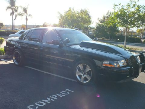 2003 Ford Crown Victoria - Sunlit driver-side profile of a dropped black sedan; chrome grille guard peeks at the front bumper.