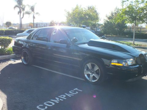 2003 Ford Crown Victoria - Black full-size sedan sits low over a COMPACT marking, amber marker glowing under the morning sun.