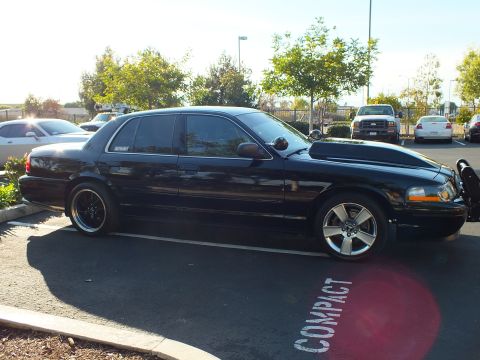 2003 Ford Crown Victoria - Profile of a low black sedan with a MERCURY quarter-window decal and chrome grille guard at the nose.