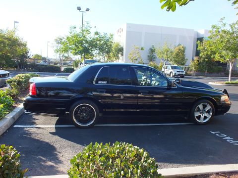 2003 Ford Crown Victoria - Glossy black full-size sedan profile with a MERCURY quarter-window decal, parked over a COMPACT marking.