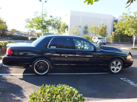 2003 Ford Crown Victoria - Rear three-quarter of a low black sedan; MERCURY quarter-window decal and dark tint catch the light.