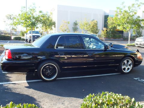 2003 Ford Crown Victoria - Low black sedan from the rear quarter, MERCURY decal on the glass and machined-lip wheels under the arches.