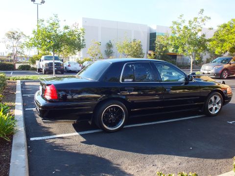 2003 Ford Crown Victoria - Rear-quarter shot of a glossy black full-size sedan sitting low across the painted parking line.