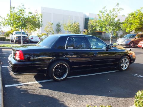 2003 Ford Crown Victoria - Rear-quarter view of a low black full-size sedan, MERCURY window decal and machined-lip black wheels in view.