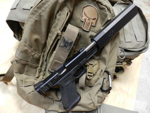1996 Ford Bronco - A tactical pistol with a suppressor is placed on a tan backpack adorned with patches and carabiners.