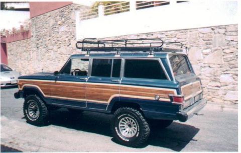 1989 Ford Bronco - This Jeep Grand Wagoneer features classic wood paneling and a roof rack, seen from a 3/4 front angle.
