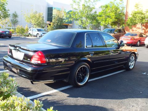 2003 Ford Crown Victoria - Lowered black Crown Victoria parked outside an office building, dark wheels and dual exhaust visible.