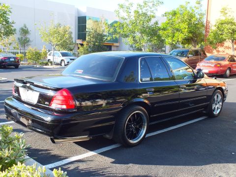 2003 Ford Crown Victoria - Glossy black Crown Victoria sedan shot from behind in a paved lot near trees.