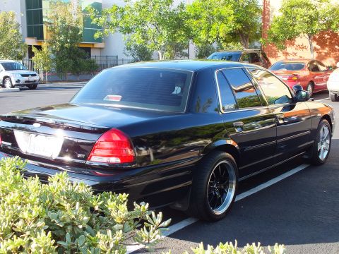 2003 Ford Crown Victoria - Black full-size Ford sedan parked nose-in, taillights and rear bumper in view.