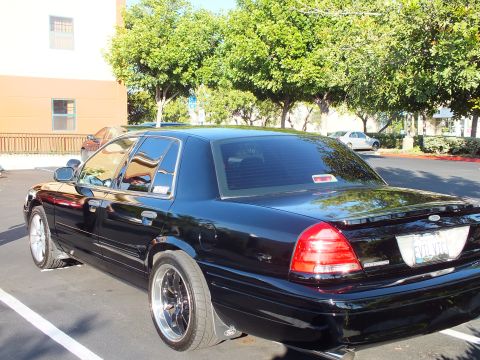2003 Ford Crown Victoria - Black Crown Victoria sedan parked beside a building, chrome-lip black wheels and tinted windows.
