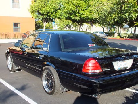 2003 Ford Crown Victoria - Lowered black Crown Victoria viewed from rear left, tail lights lit by sun.