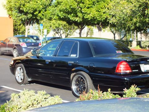 2003 Ford Crown Victoria - Side profile of a lowered black Crown Victoria sedan parked among trees.